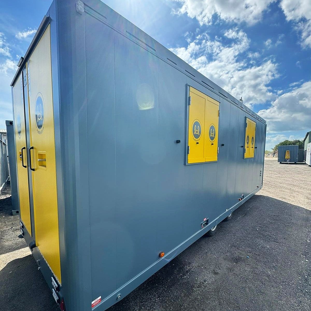 A large gray utility trailer with yellow doors and windows, featuring the U.S. Coast Guard emblem, parked on asphalt with a partly cloudy blue sky overhead.