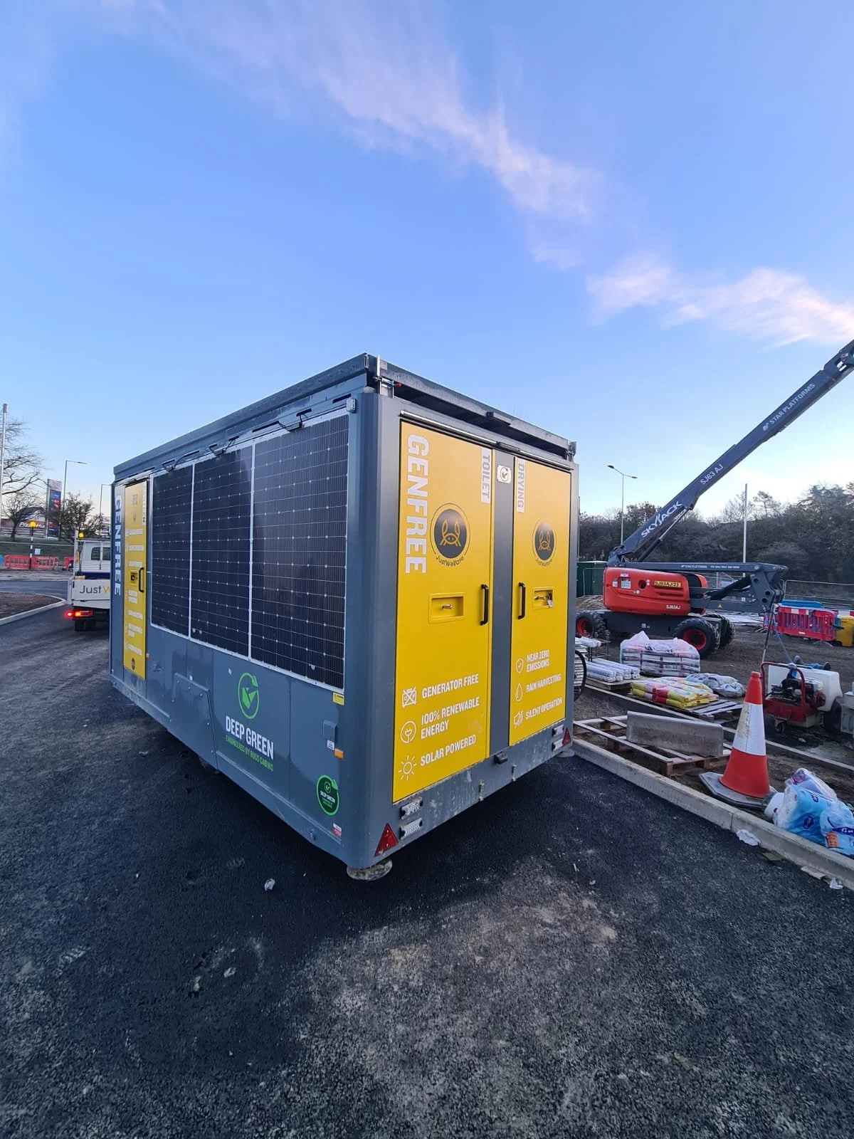 A portable generator covered with solar panels, parked at a construction site with construction equipment and orange traffic cones in the background.