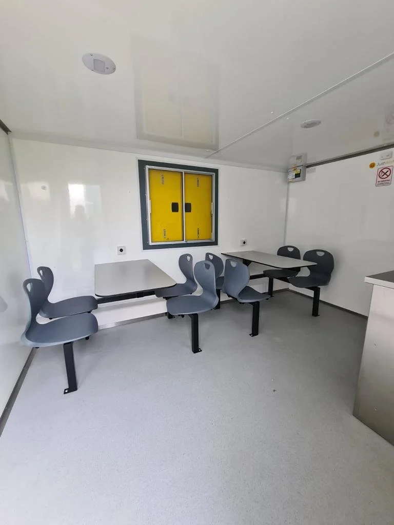 Empty room with gray chairs and tables, yellow window, and white walls.