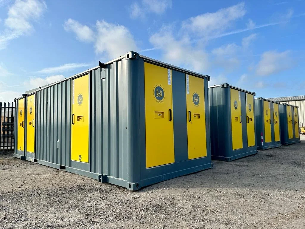Multiple yellow and gray storage containers outdoors on gravel surface under a partly cloudy sky.