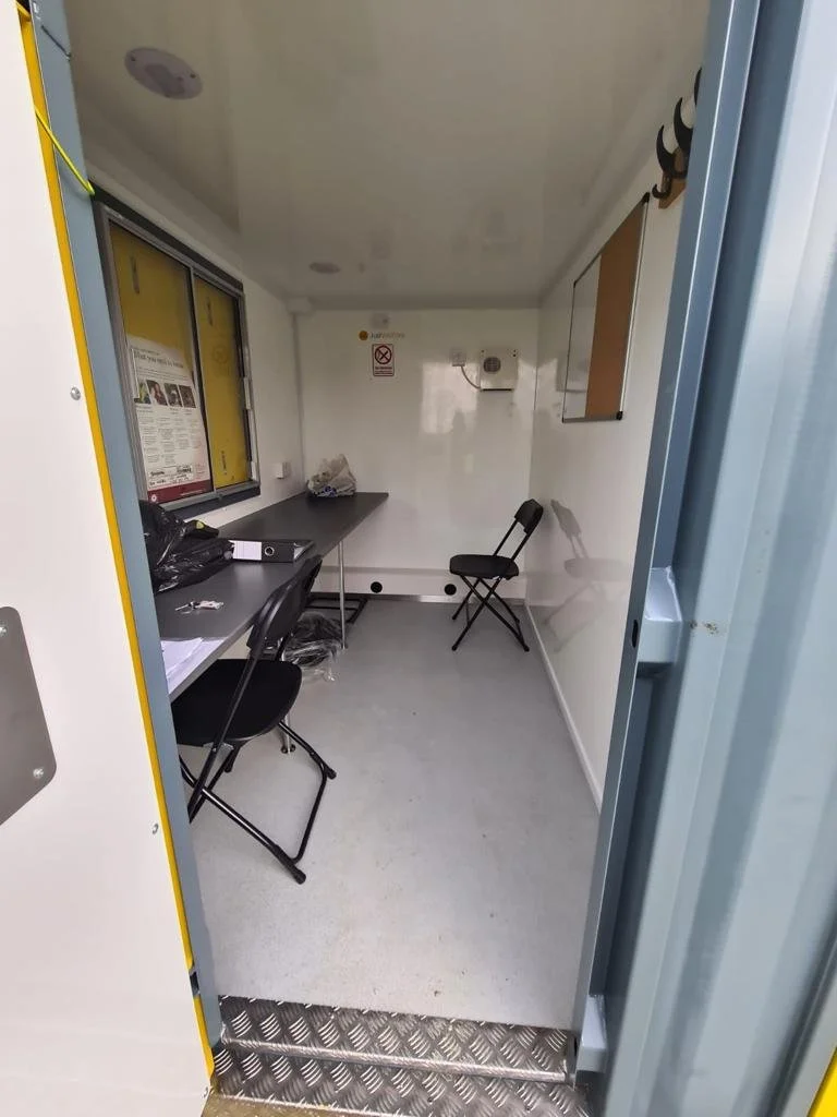 Small, plain office or security room with two black chairs, filing cabinets, a window, and a whiteboard on the wall.