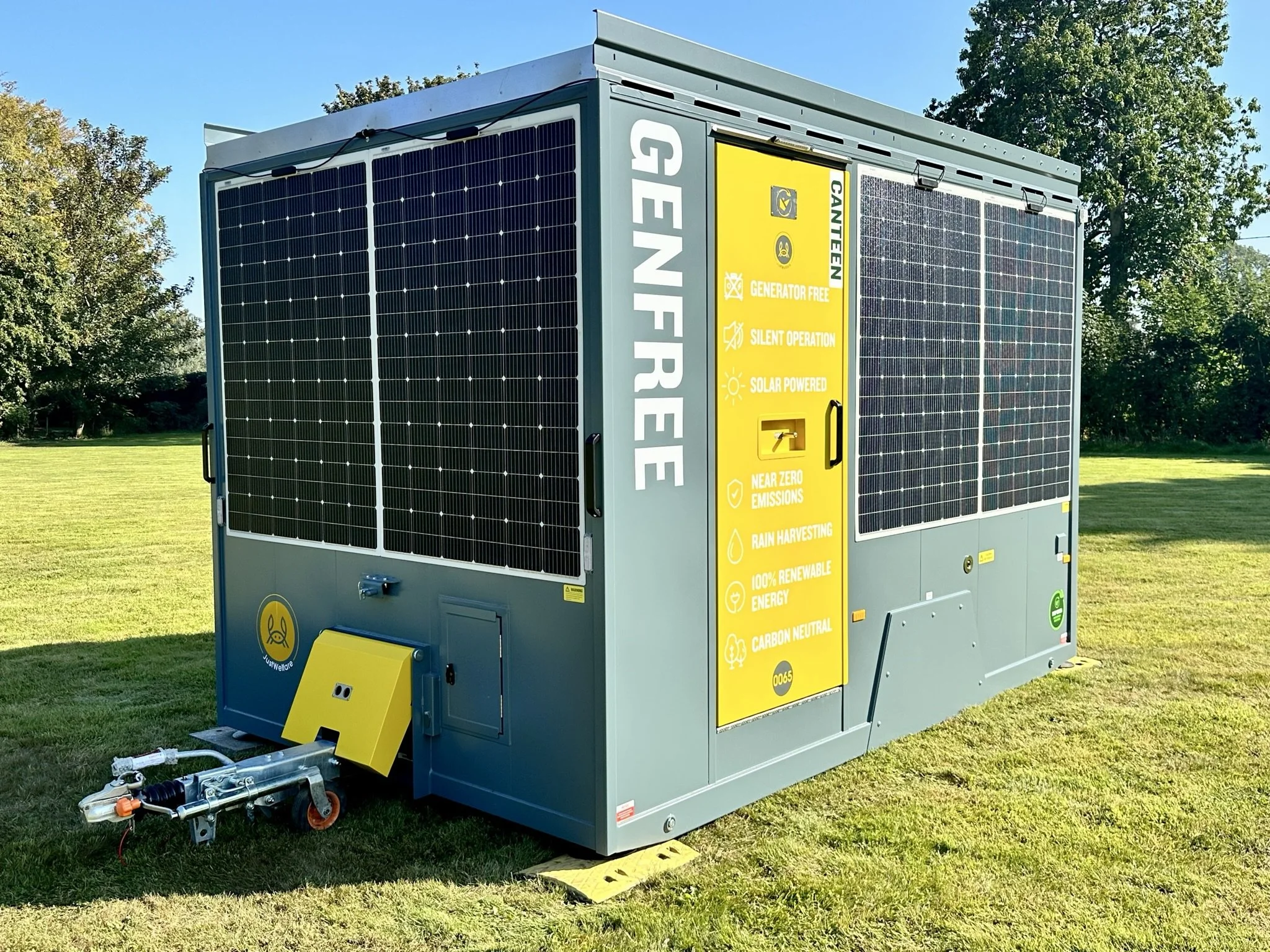 A solar-powered generator and storage unit labeled 'GENFREE,' with solar panels on its sides, situated on a grassy field with trees in the background.