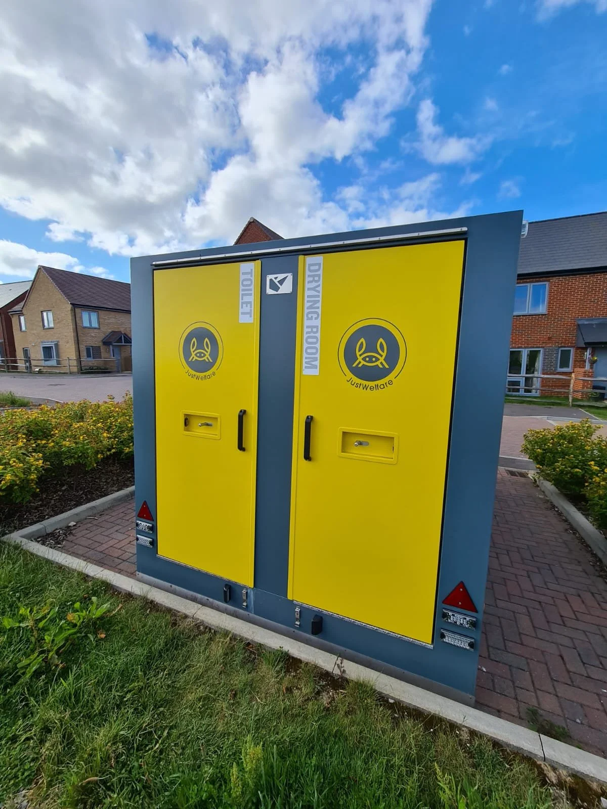 Yellow and gray public toilet and drying room lockers outdoors with a partly cloudy sky in the background.