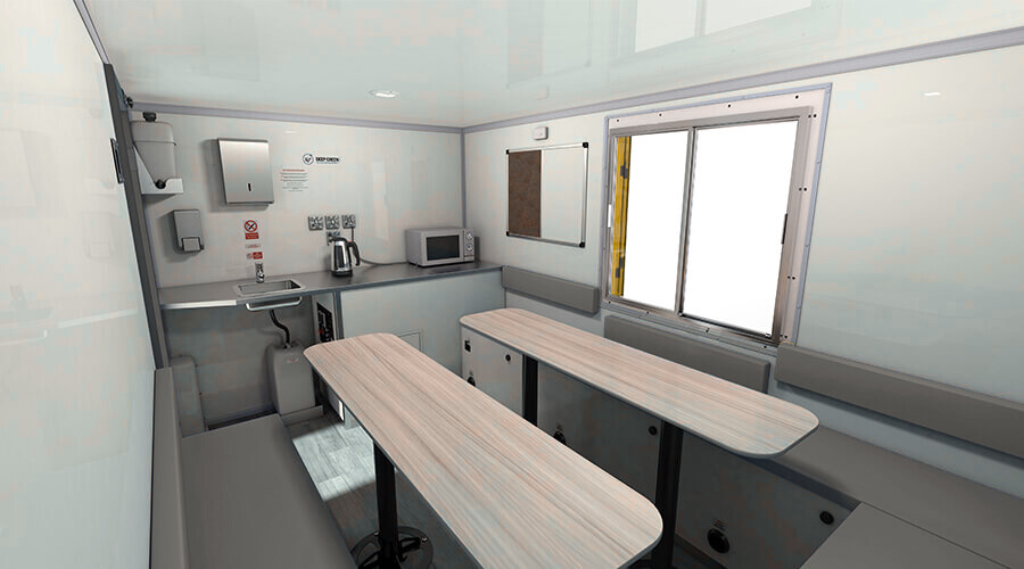 Interior of a small medical or testing mobile unit with a foldable table, microwave, kettle, sink, and windows.