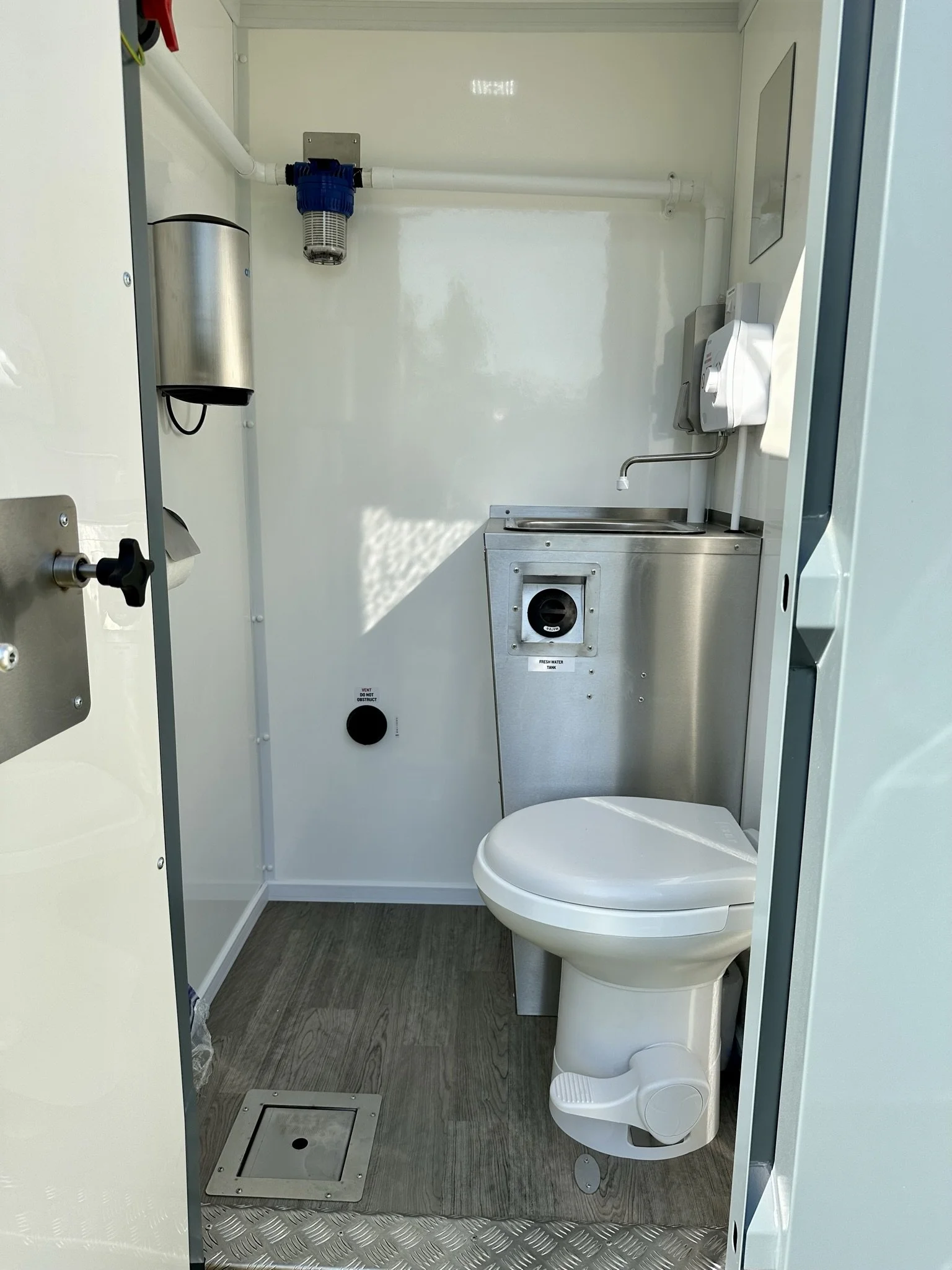 Small, mobile restroom with a toilet, sink, soap dispenser, paper towel dispenser, and water heater, in a clean, compact space.
