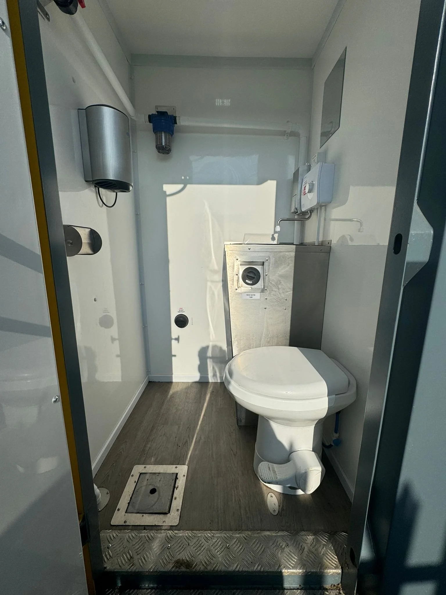 Small industrial bathroom with a toilet, stainless steel sink, and various plumbing fixtures.