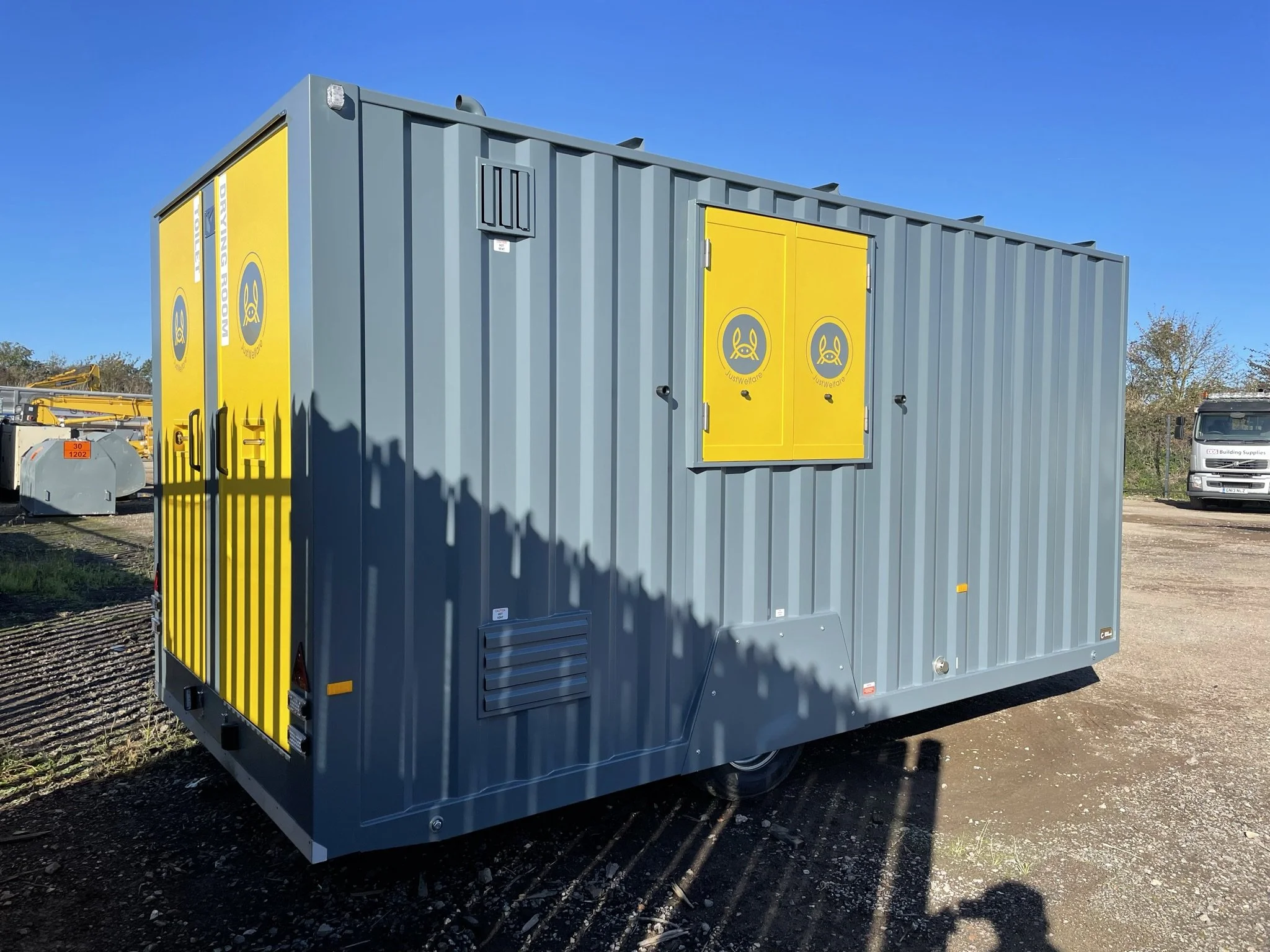 A large blue and yellow portable generator or equipment container outdoors on dirt, with tools and machinery in the background under a clear blue sky.