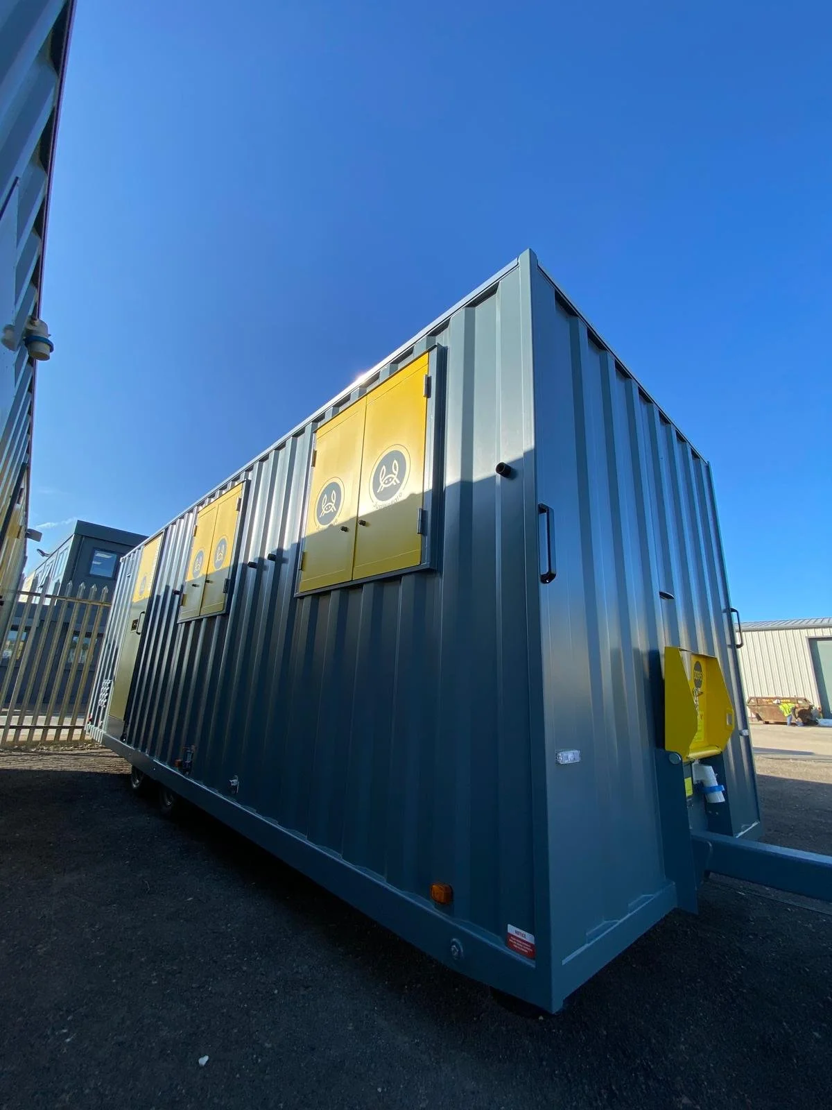 A large gray modular container with yellow compartments and gray doors, set outdoors under a clear blue sky.
