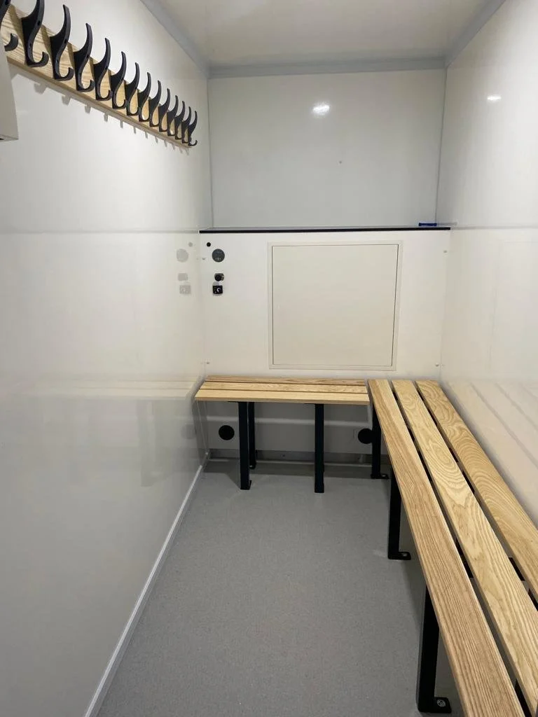 Empty white room with a wooden bench and hooks for shoes on the wall.