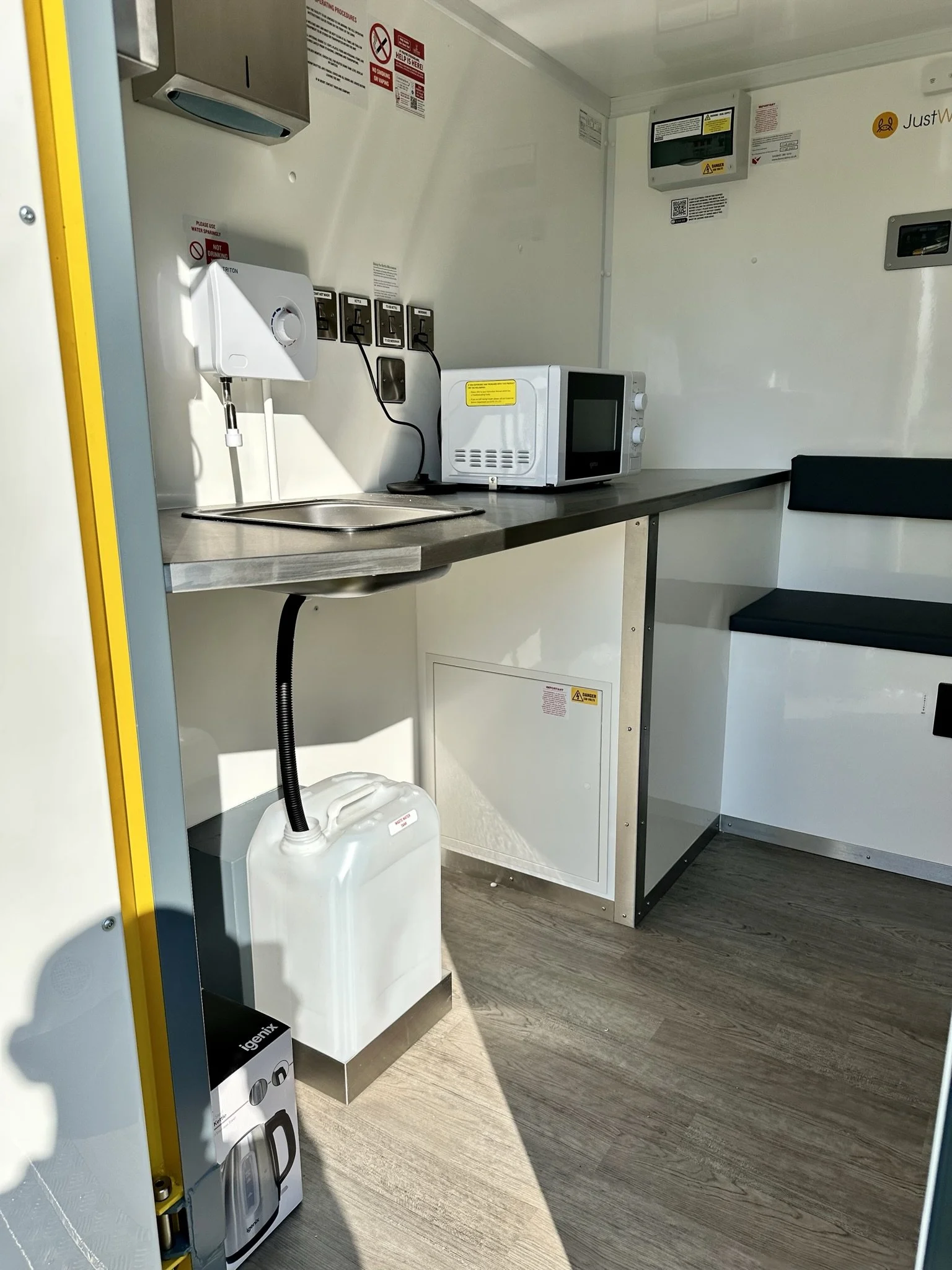 Interior of a food truck kitchen with a microwave, water sink, and various outlets and safety posters.
