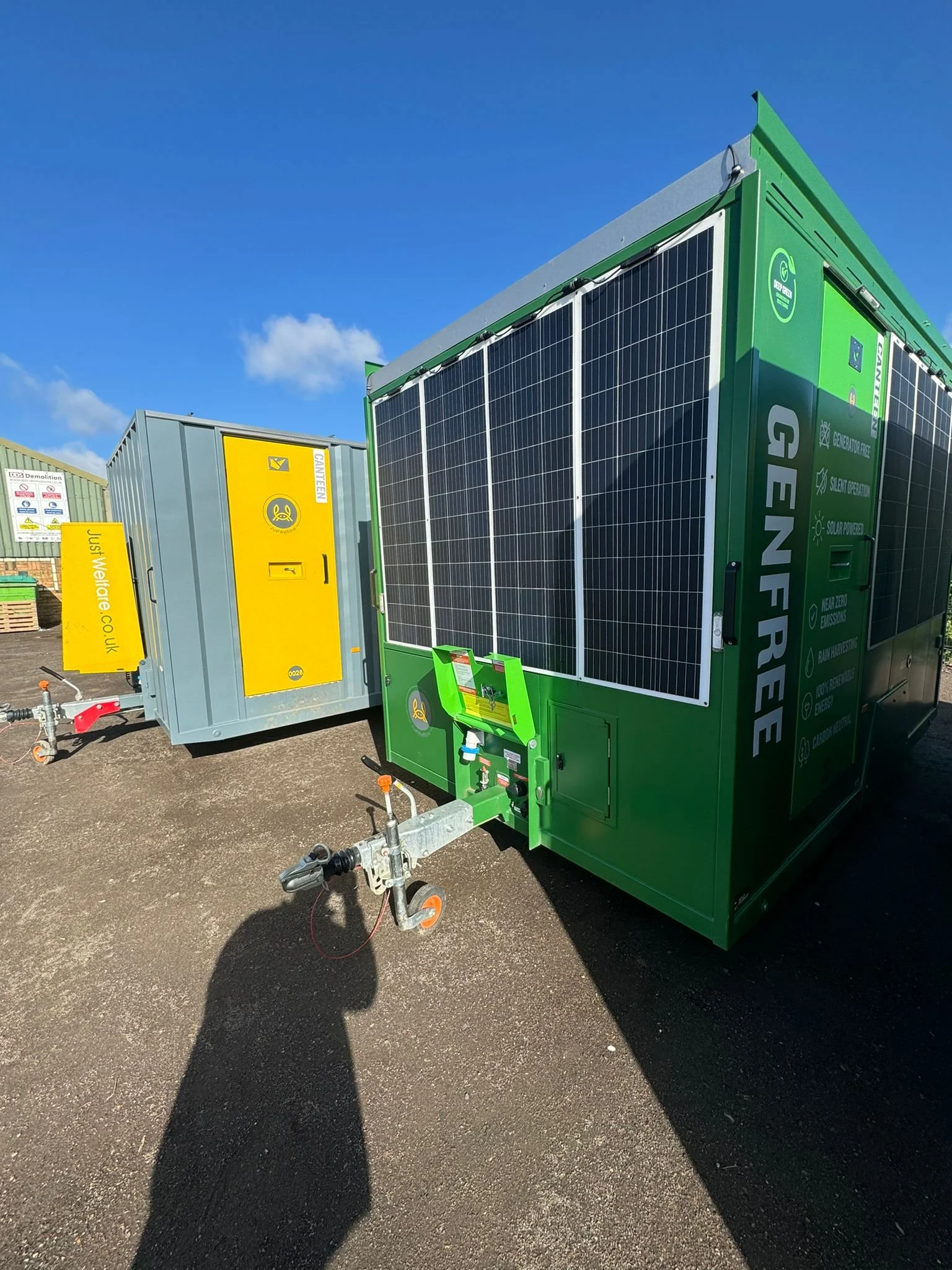 Green mobile generator with solar panels parked on asphalt with a blue sky background.