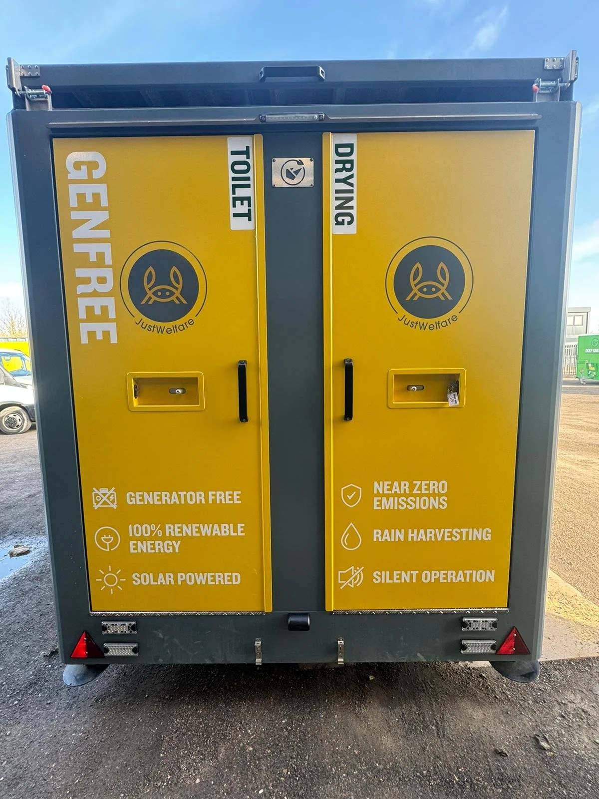 A yellow and gray outdoor electric vehicle charging station with labels indicating it is generator free, 100% renewable energy, solar powered, near zero emissions, rain harvesting, and silent operation.