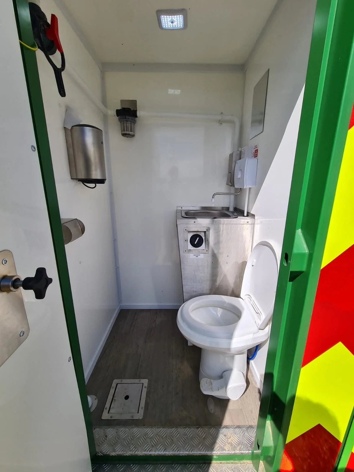 Small bathroom with a toilet, stainless steel sink, wall-mounted paper towel dispenser, soap dispenser, and an air dryer, with a light on the ceiling.