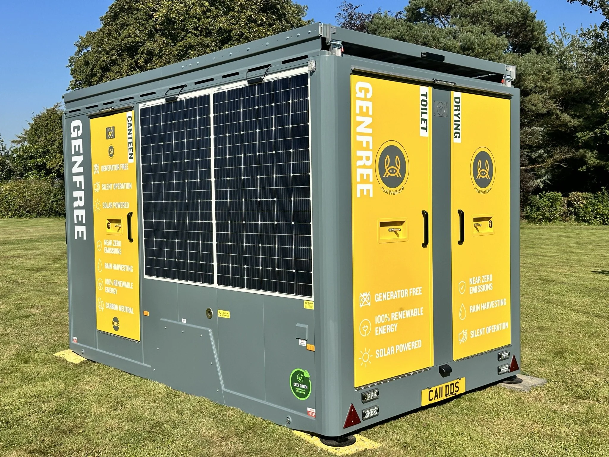 A solar-powered generator unit with yellow and gray panels, located outdoors on a grassy field with trees in the background.