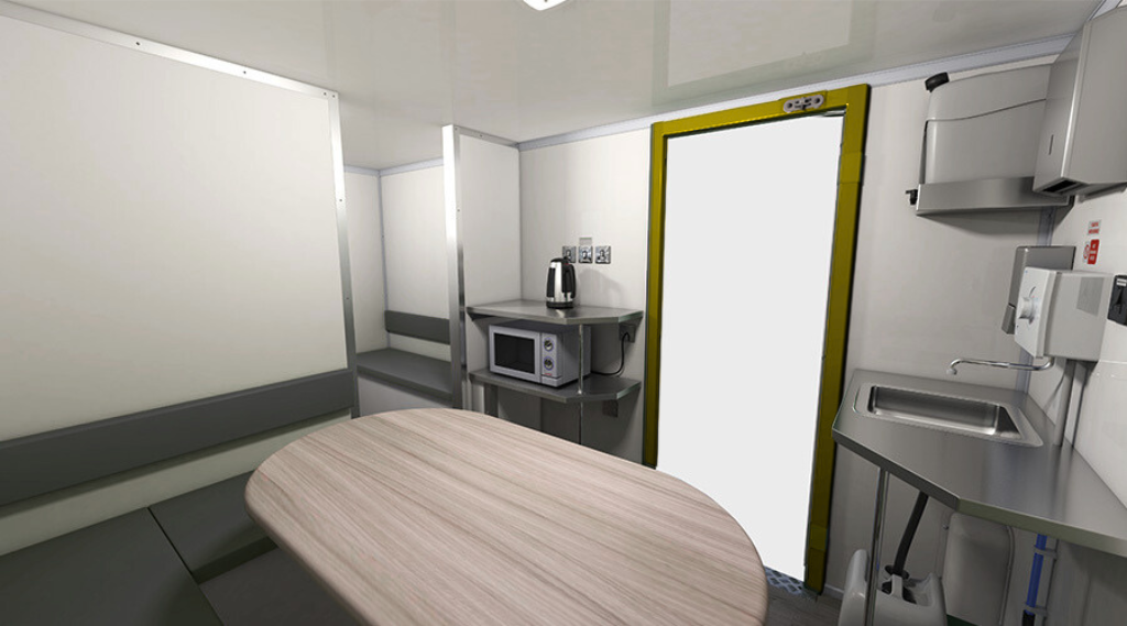 Small kitchen in a compact space with a microwave, kettle, sink, and a door with yellow trim.