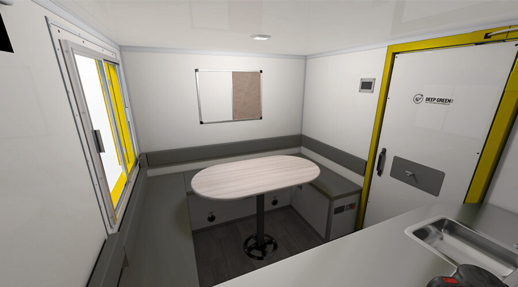 Interior of mobile or portable medical or quarantine unit with white walls, a small table, gray cushioned seating along the wall, a window with yellow frame, and a door labeled 'Deep Green'.