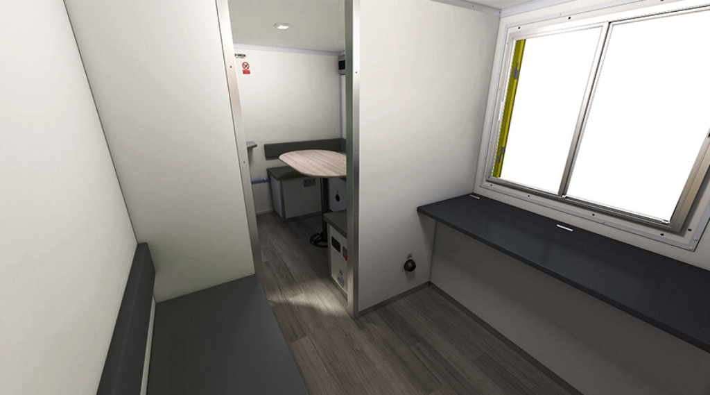 A small, clean, temporary medical or examination room with white walls, a window with a black sill, and a black bench. There is a folding partition separating the main area from a small alcove with a table and a chair, likely for medical purposes.