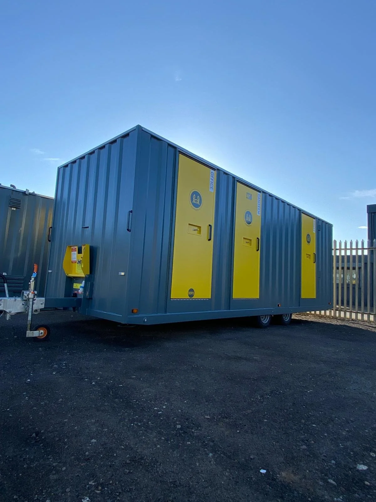 A large mobile hazardous waste storage trailer with yellow doors and biohazard symbols, parked on a paved lot under a clear blue sky.
