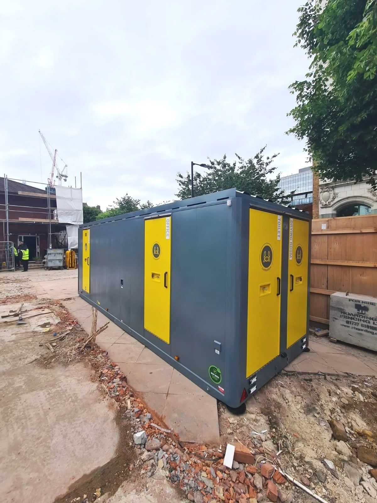 A mobile restroom trailer with yellow doors and black symbols, situated on a construction site.