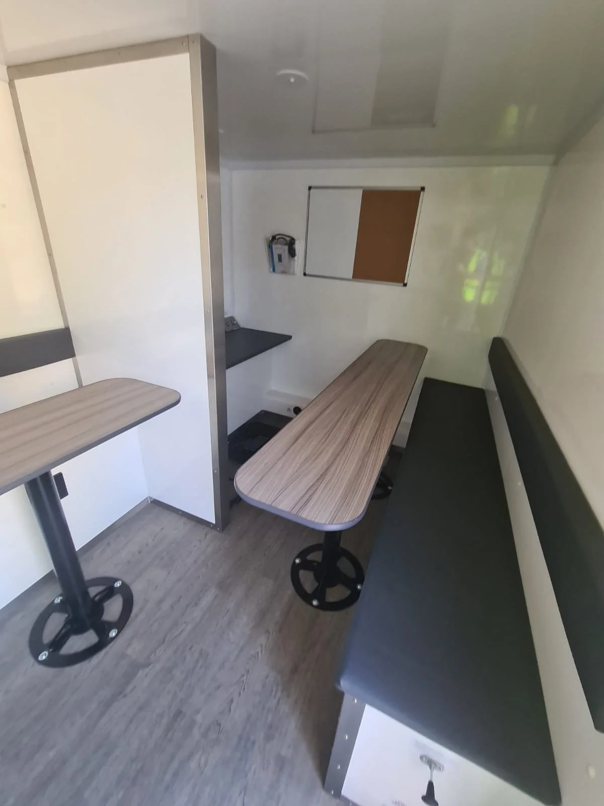 Interior of a small room with two small round tables, a black bench seat, and a white cabinet, with a small window, a wall-mounted device, and a safety lock on a cabinet