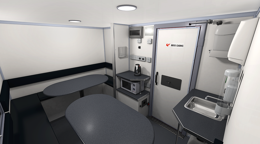Interior of a small mobile office or workspace with tables, a microwave, a kettle, a sink, and various electrical panels.