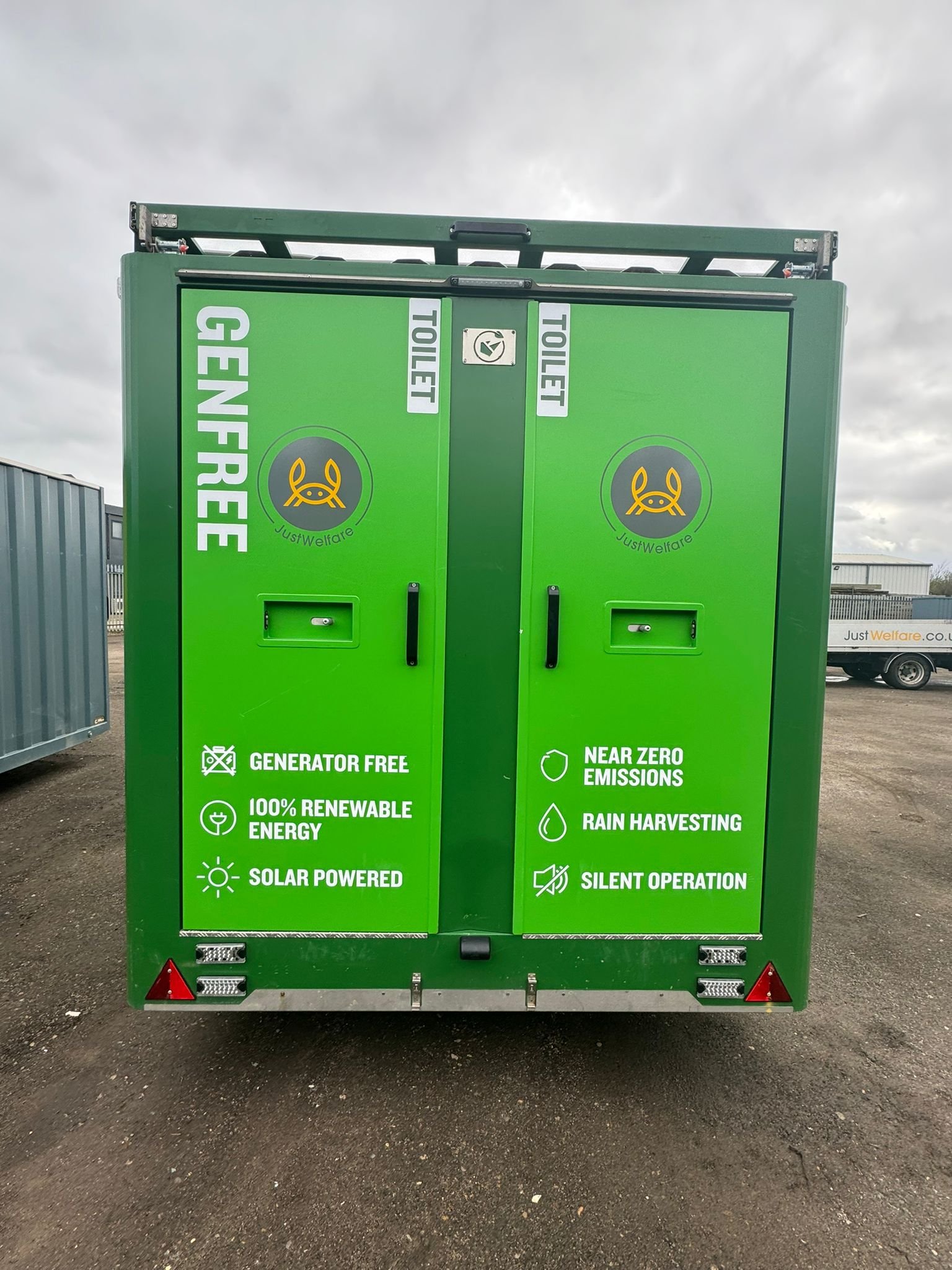 Green vehicle with signage promoting eco-friendly features, including generator free, 100% renewable energy, solar powered, near zero emissions, rain harvesting, and silent operation, parked outdoors with an overcast sky.