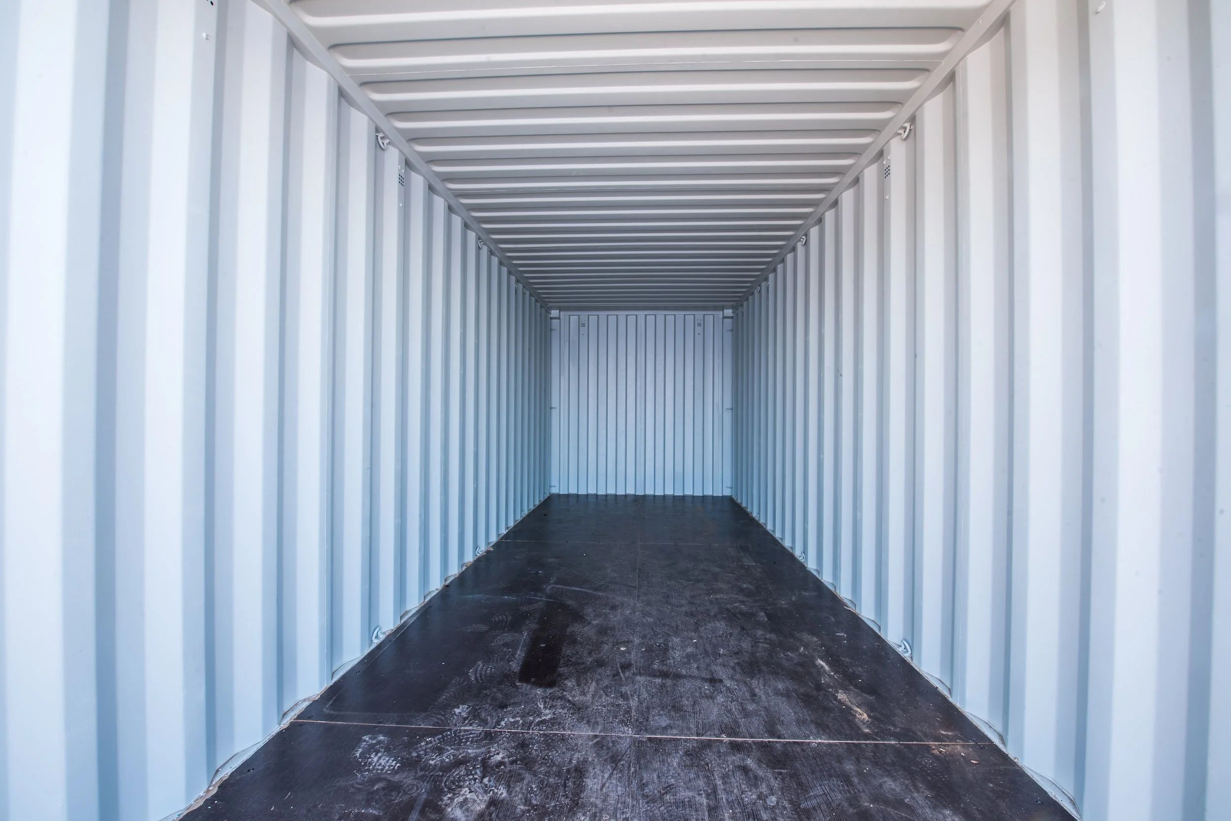 Empty metal storage container with corrugated metal walls and ceiling, and a wooden floor.