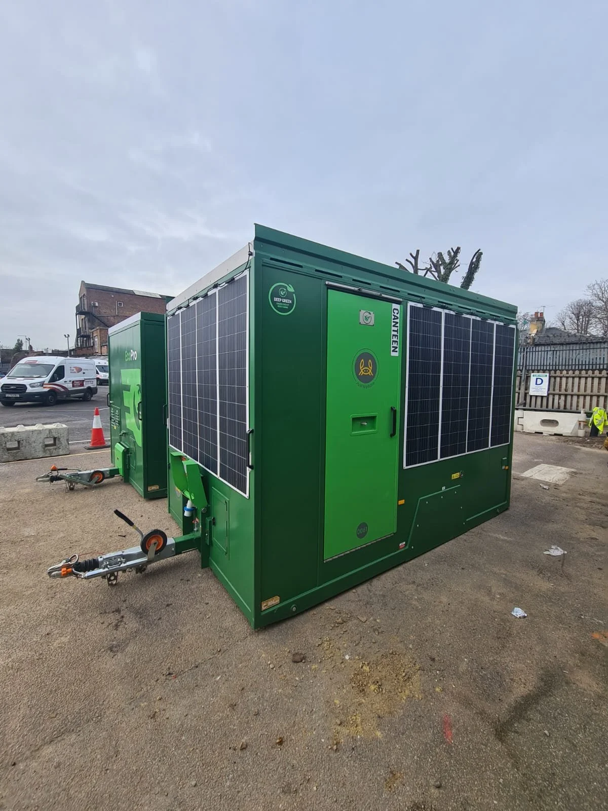 Green electrical equipment with solar panels installed, parked outdoors on a paved area.