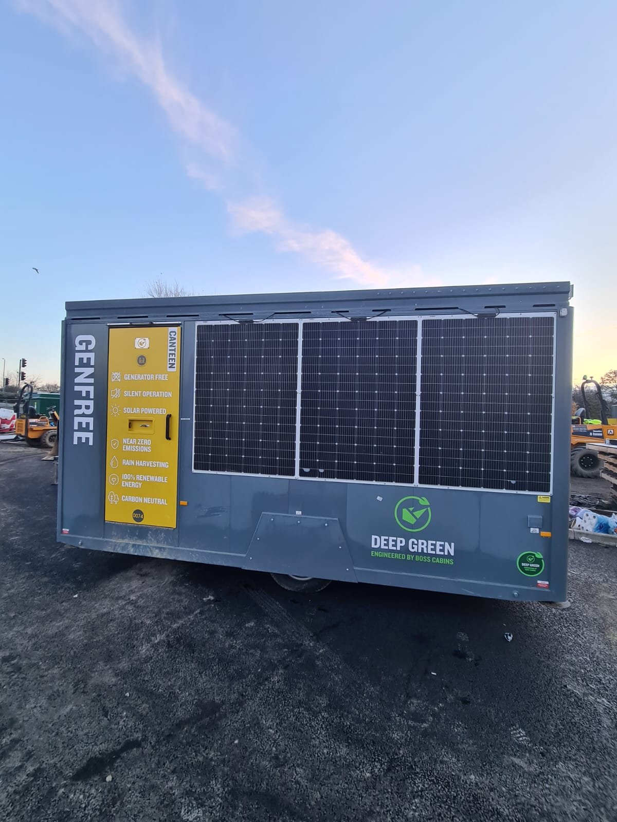 Portable solar power generator with solar panels on top, labeled with features like generator free, silent operation, solar powered, near zero emissions, rain harvesting, 100% renewable energy, and carbon neutral, at a construction site during evenin