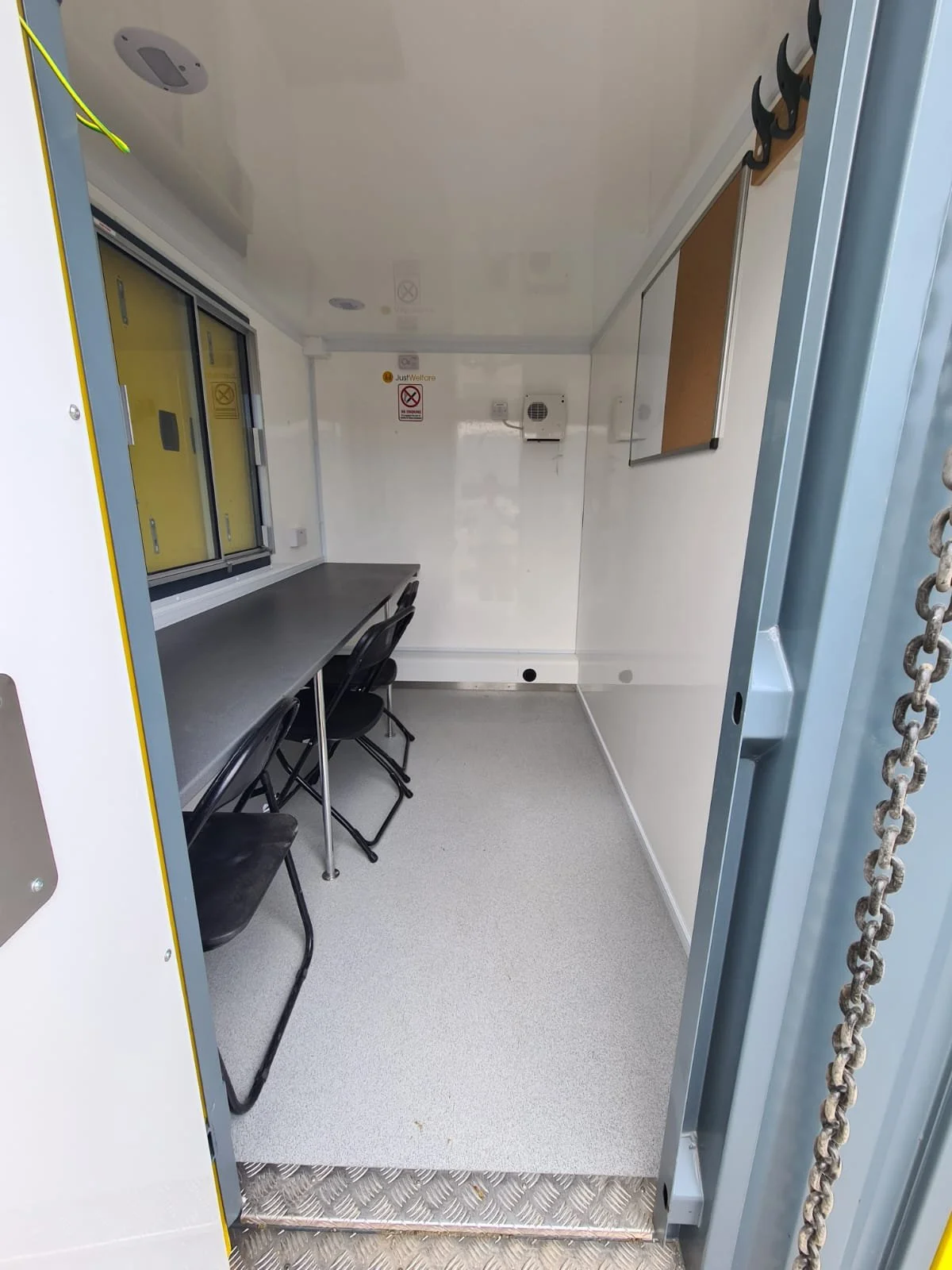 Empty mobile command center or mobile office with a long table, three chairs, a window, wall-mounted hooks, and equipment.