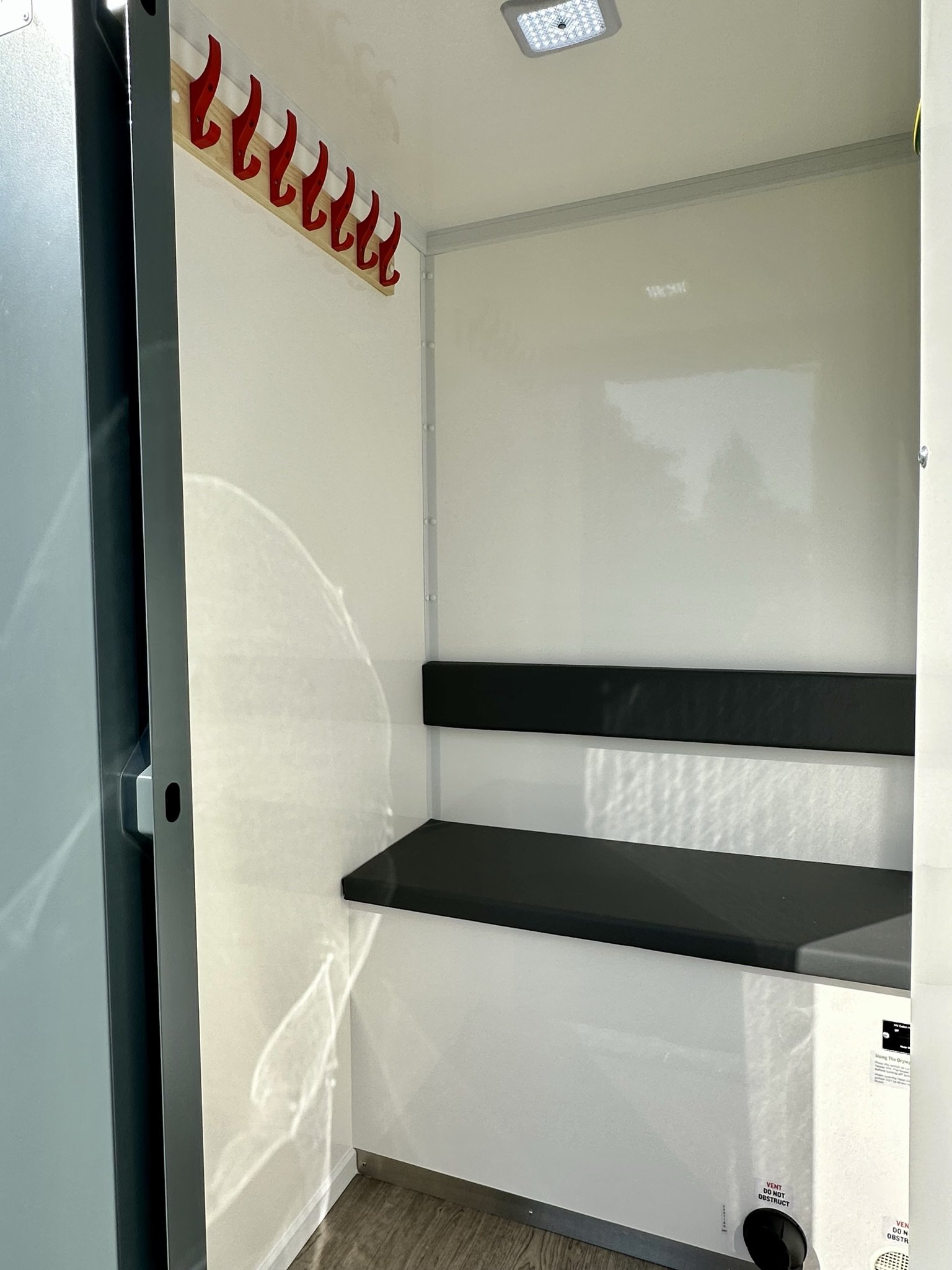 Empty hospital or medical capsule with black cushioned bench and coat hooks mounted on the wall.