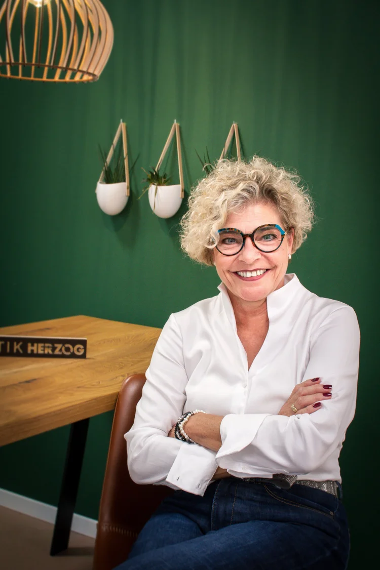 Petra Huber, Fachberaterin Augenoptik, lachend vor grüner Wand