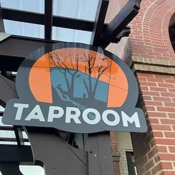 Sign for TAPROOM with a silhouette of trees against an orange sunset background.