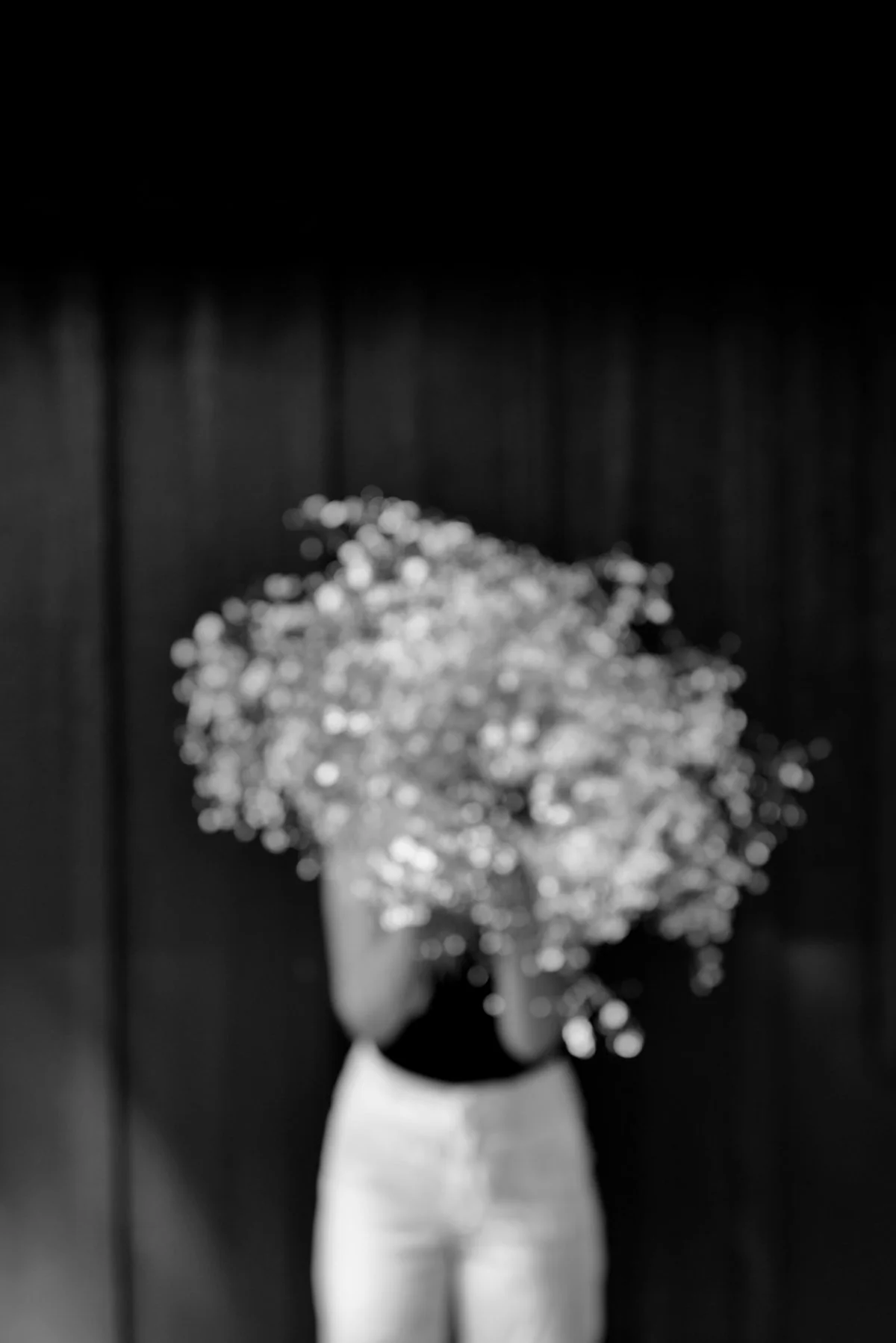 Abstract black and white photograph of a person holding a bunch of flowers in front of their face, with a blurred background.