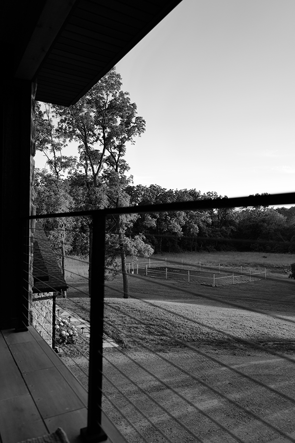 View of a rural landscape from a balcony, featuring trees, grass, and fences.