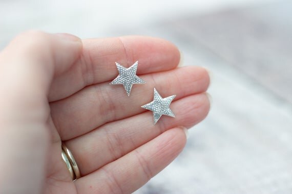 5 pointed silver star stud earrings held in a hand for scale