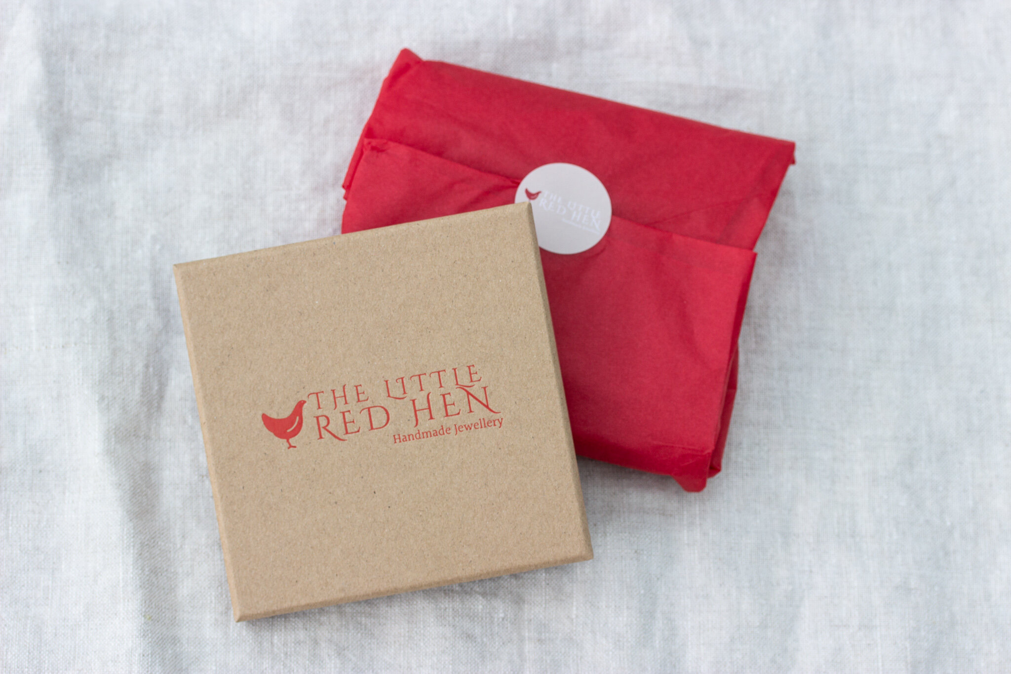 square kraft gift boxes by the little red hen jewellery with red logo and red gift wrap tissue