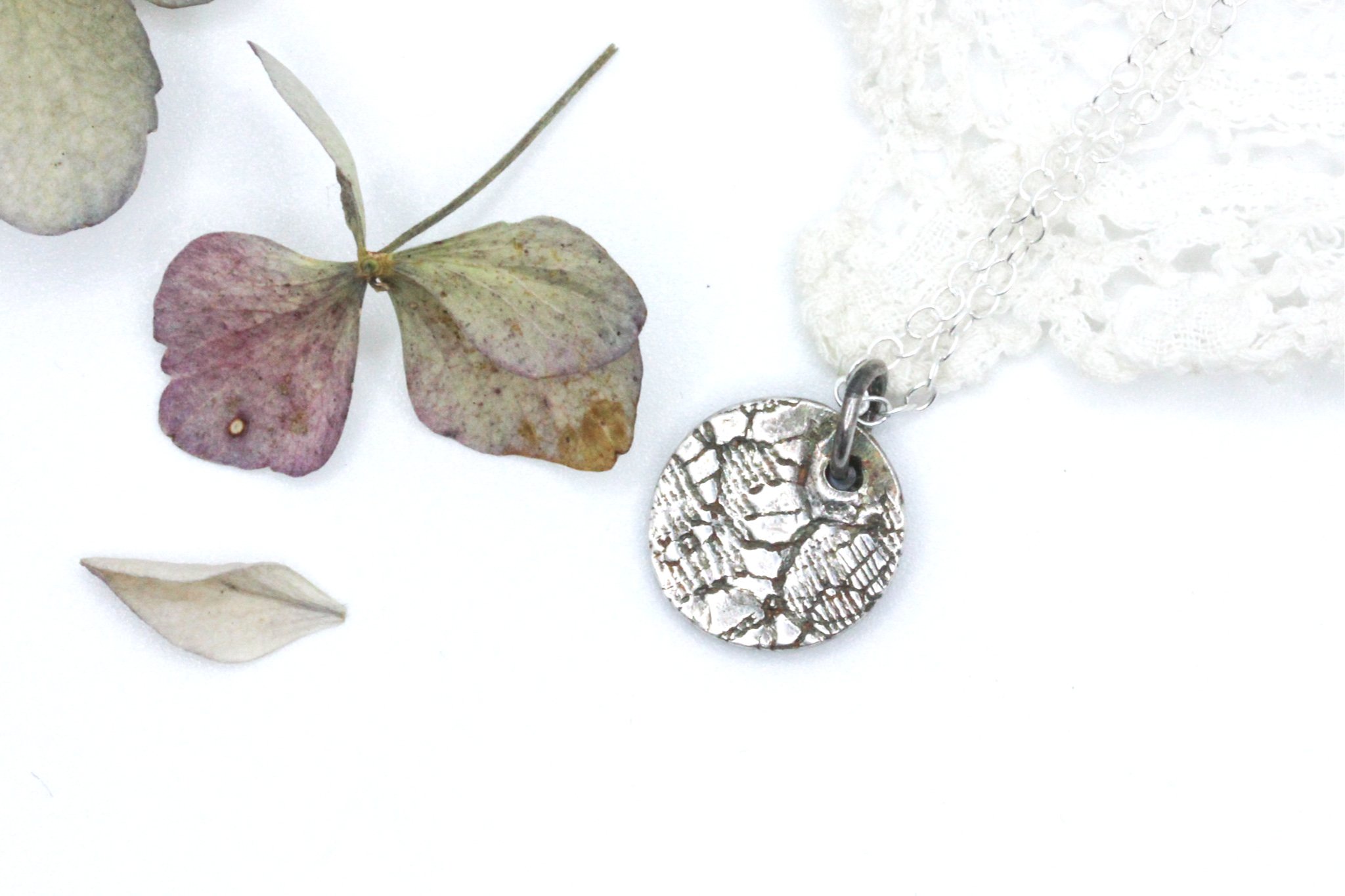 small silver circle shaped pendant with lace pattern