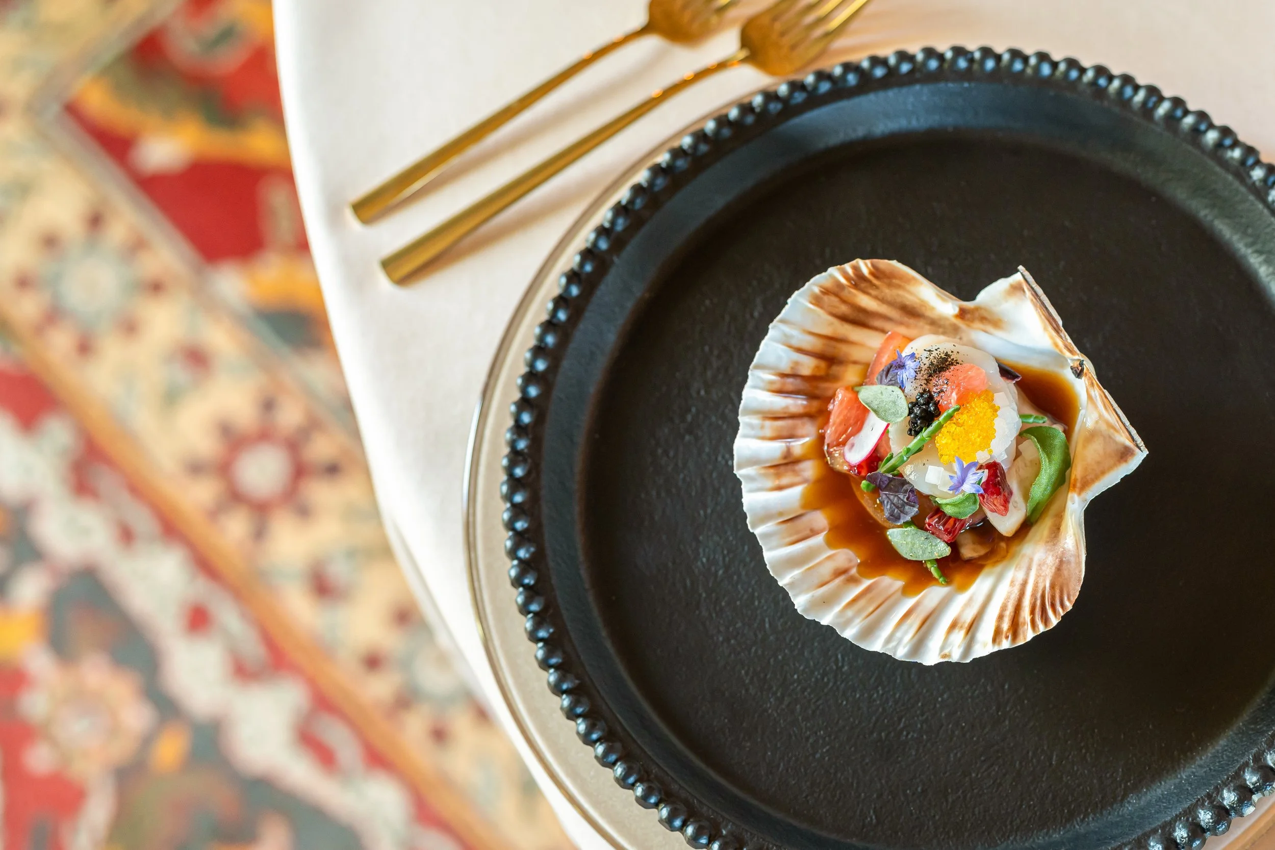 Colourful scallop dish presented in a shell with caviar
