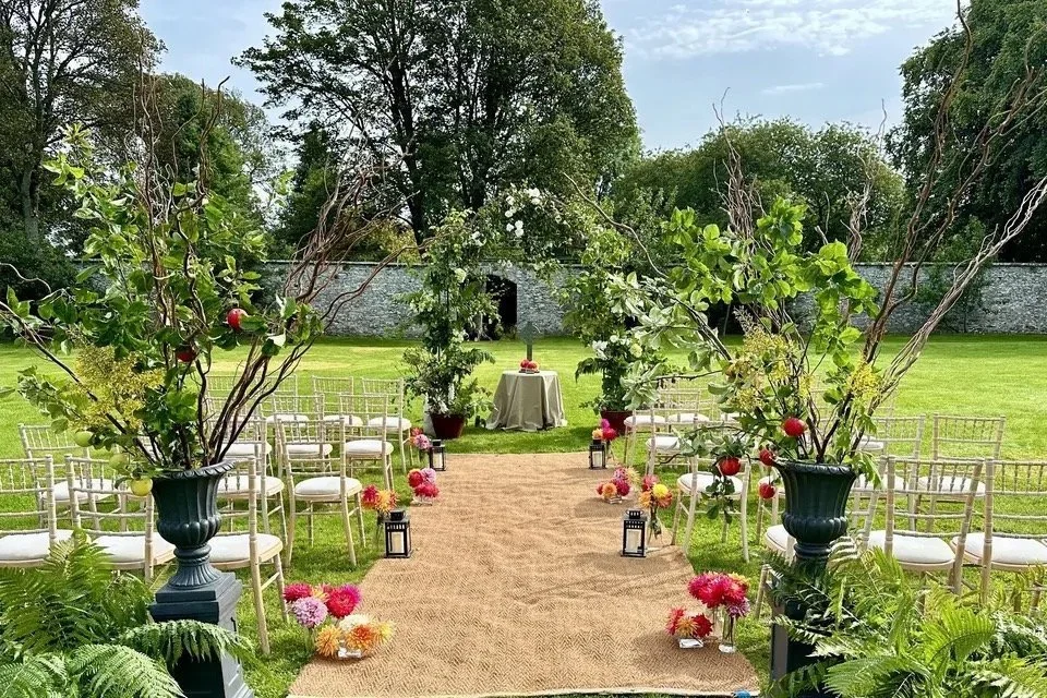 Outdoor wedding ceremony setup with chairs, greenery, and floral decorations on a grass lawn.