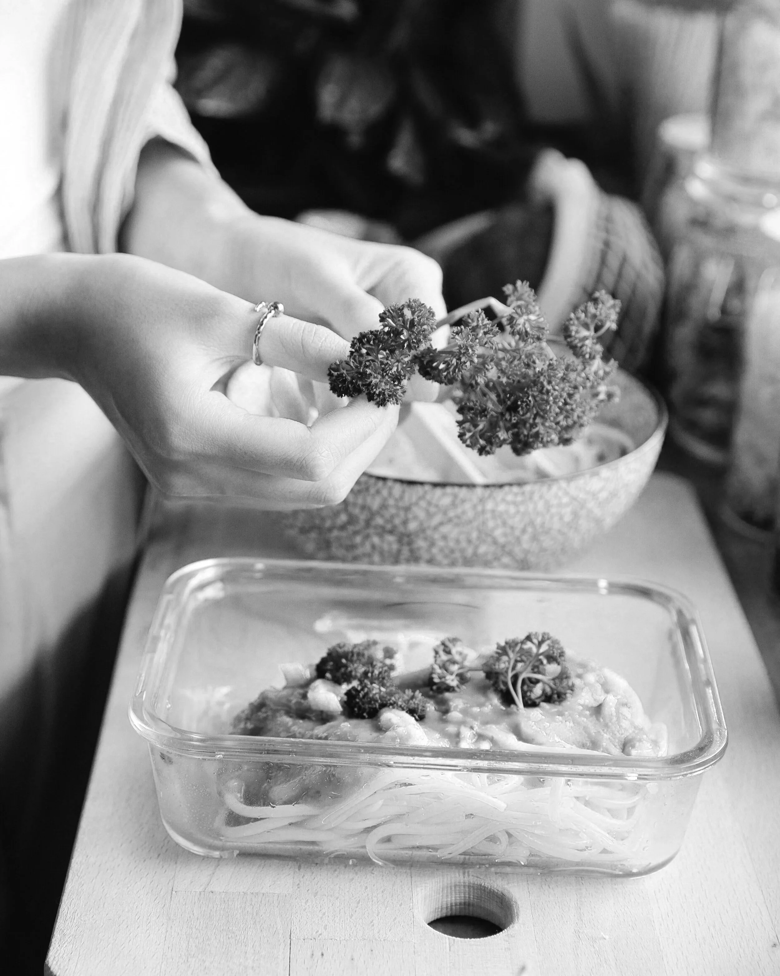Close-up of a meal prep chef holding a piece of broccoli. In the background, there is a container with more broccoli and a pot or bowl.