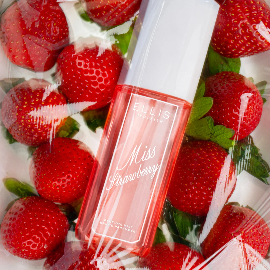 A bottle of Ellis Brooklyn Miss Strawberry Perfume Mist inside a package of fresh strawberries.