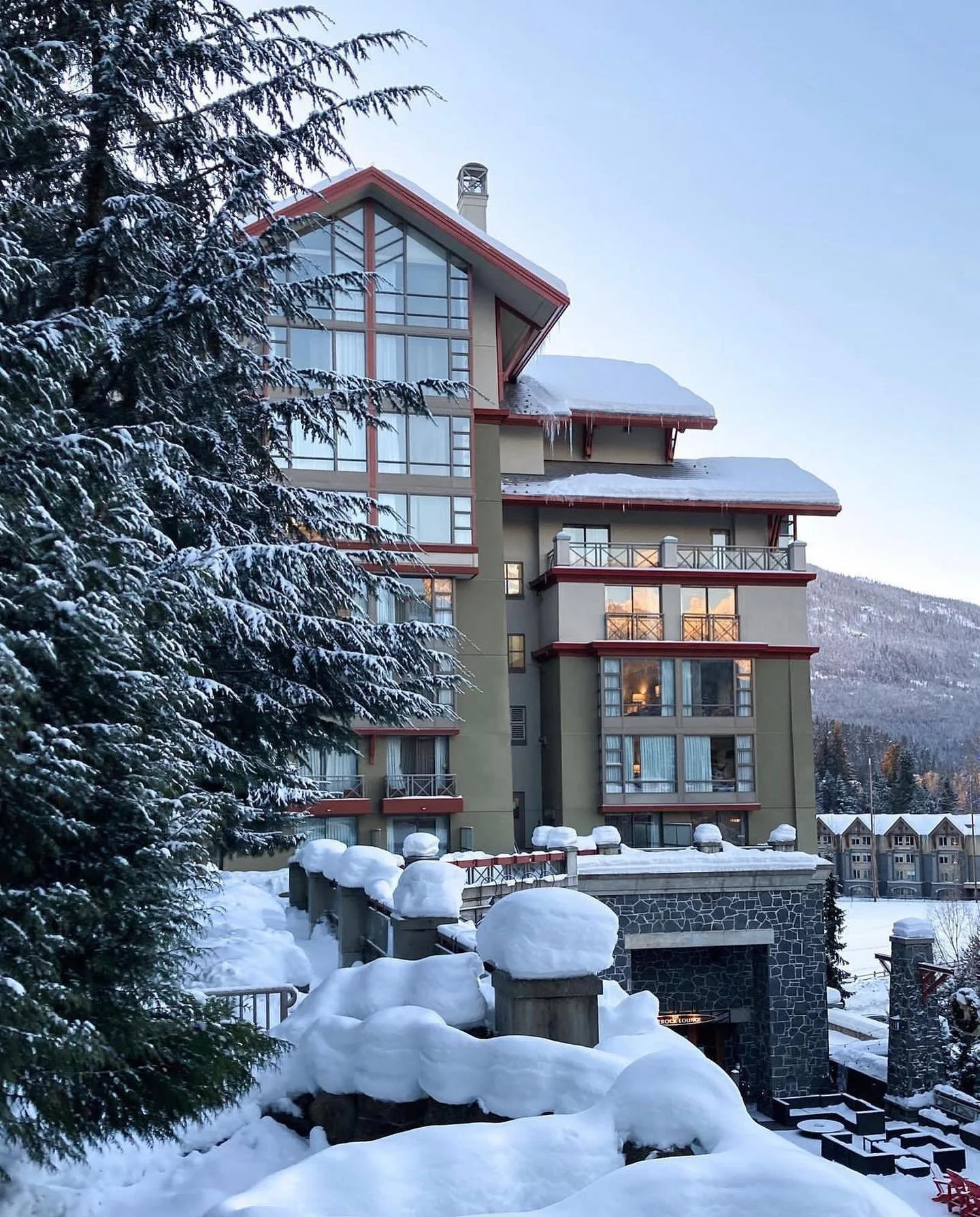 Edificio de varias plantas en un paisaje nevado, con árboles cubiertos de nieve en primer plano y montañas al fondo