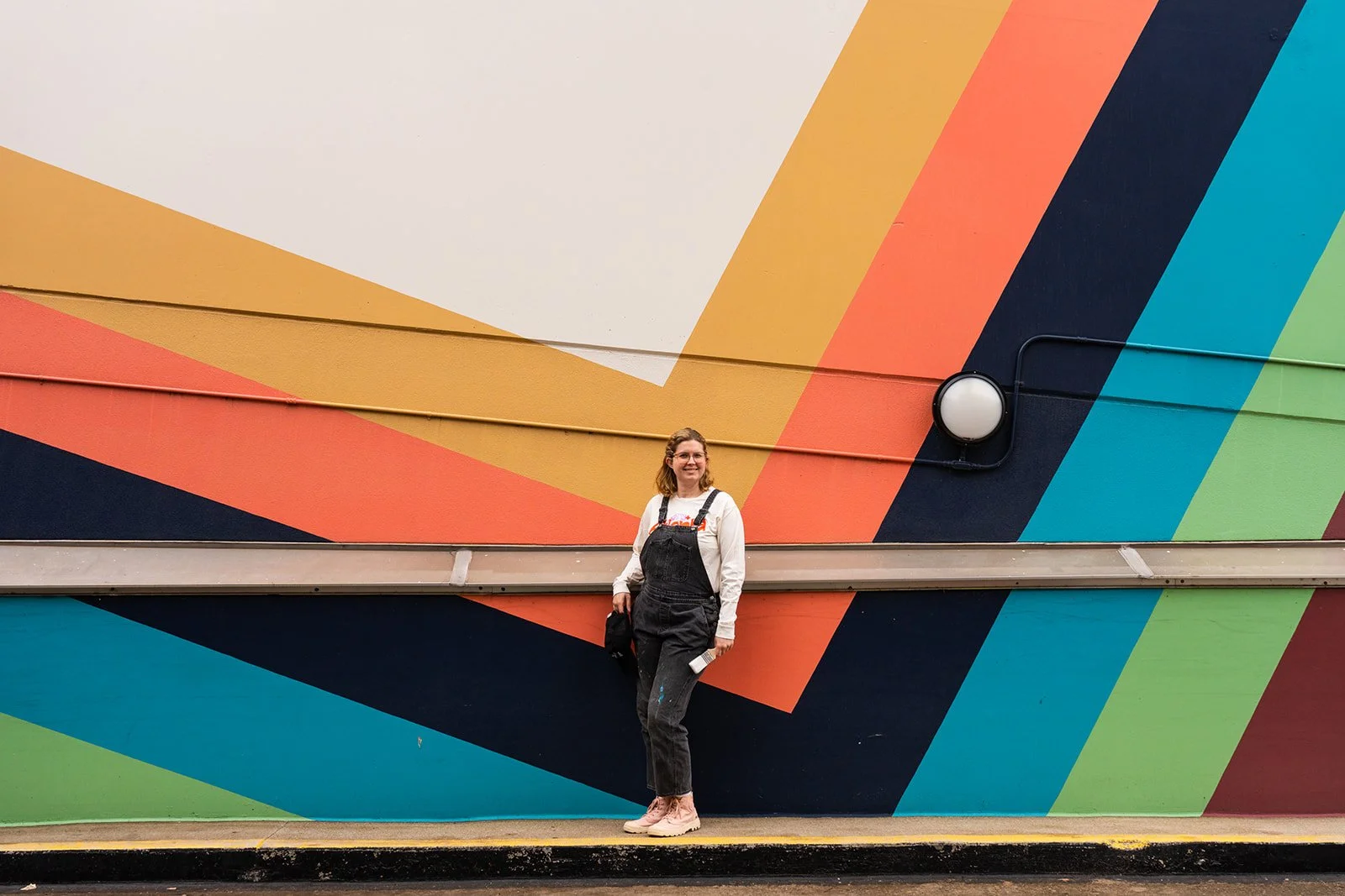 Elaine standing in front of a colorful striped mural she painted at Atlantic Station