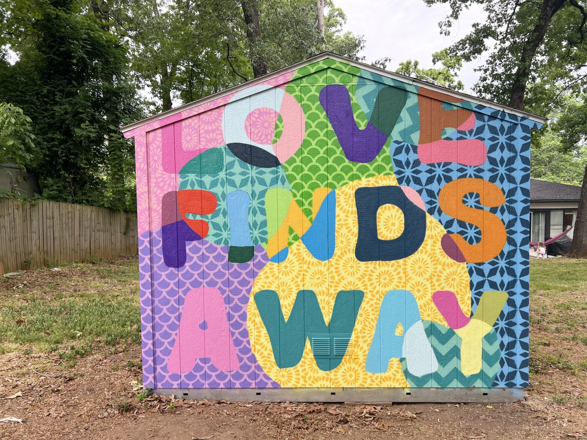 Love Finds A Way. Brightly colored mural with bold lettering and patterns on an outdoor shed. 2026