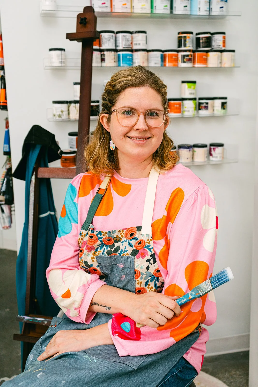 Elaine sitting in an art apron and holding a paintbrush