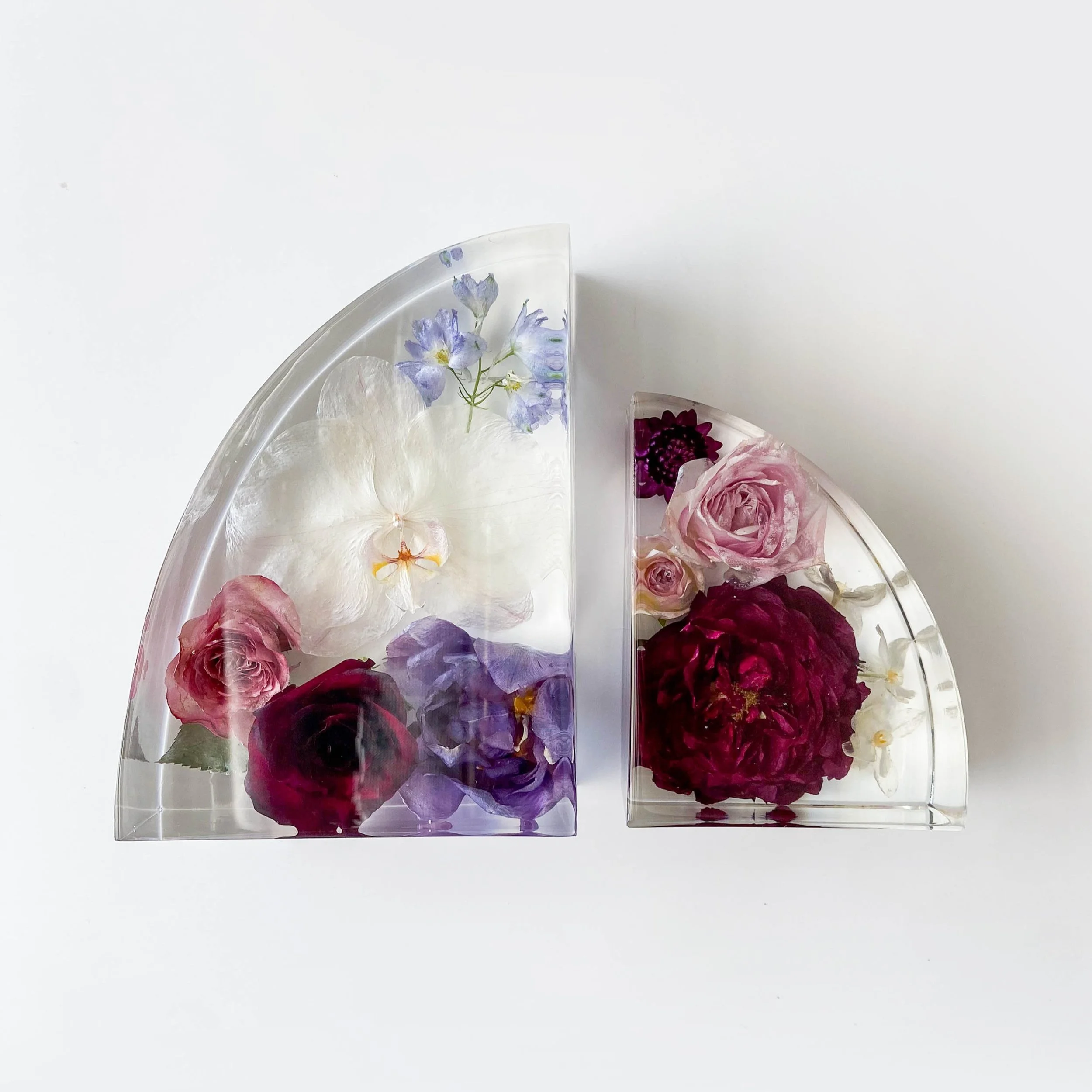Shown is a small and large bookend together with purple, white and red flowers inside. This shape is best described as a half arch - think a hard 90 degree angle and then an arch connecting the two points, they're intended to sit on a bookshelf
