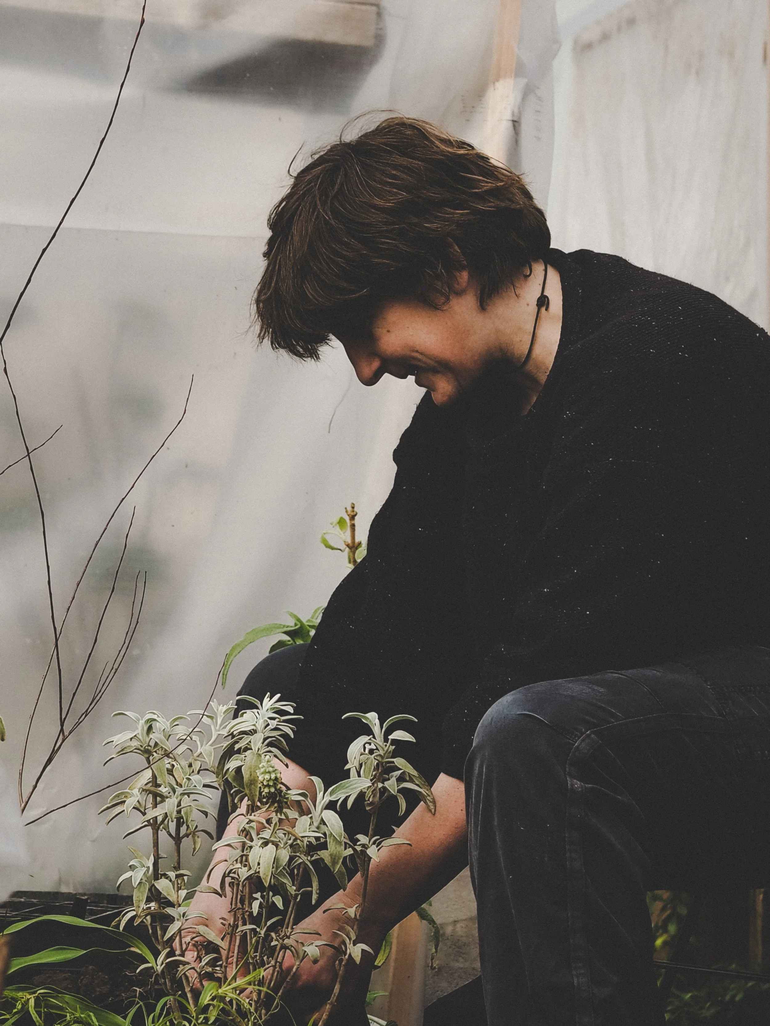 A person kneeling down and tending to plants in a garden or greenhouse.