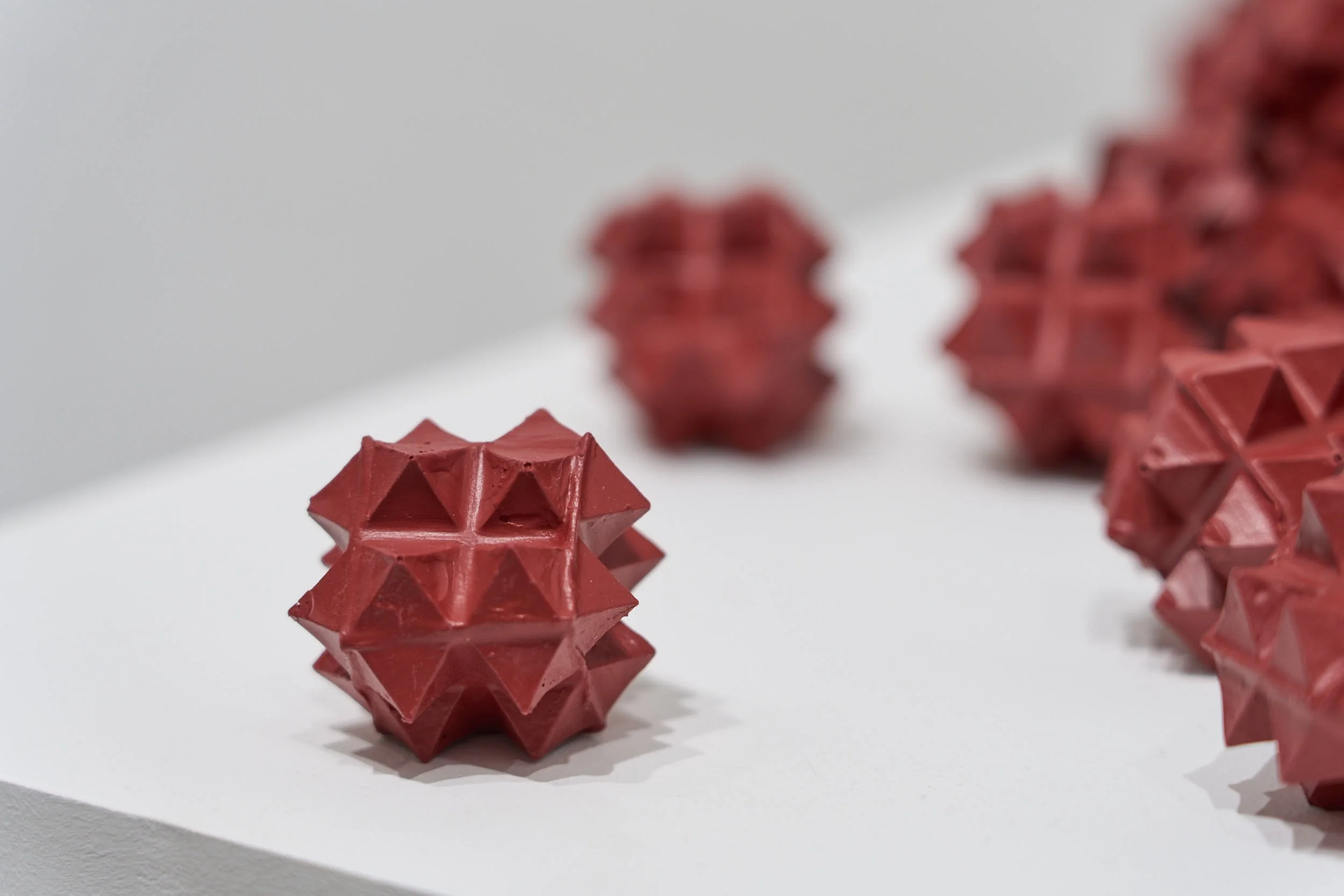Group of red, spiky, geometric sculptures made entirely from acrylic paint, on a white surface, with one sculpture prominently in the foreground and others blurred in the background.