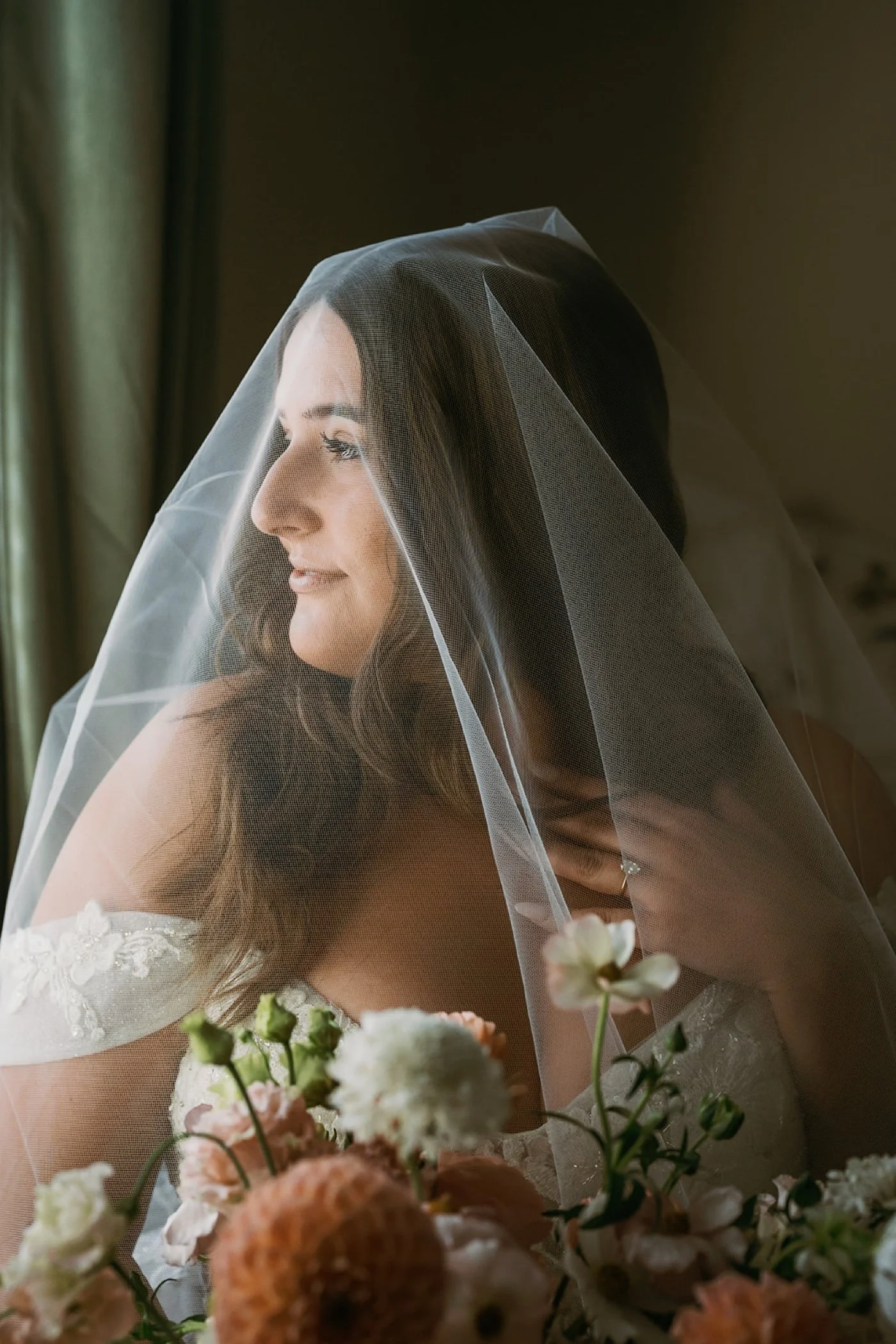 bride with a bouquet of flowers wearing a veil and looking out of a window